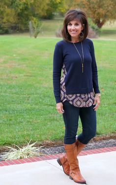 a woman standing in front of a green field wearing brown boots and a black top