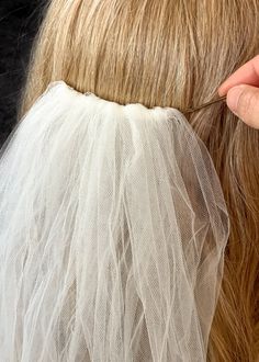 a woman is getting her hair done with a piece of white veil on top of her head