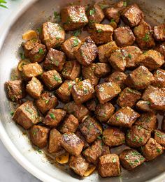 cooked meat cubes in a pan with parsley on top and seasoning sprinkled around the edges