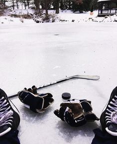 two pairs of ice skates sitting on top of snow covered ground next to a hockey stick