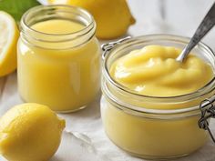 two jars filled with lemon custard on top of a white cloth next to sliced lemons