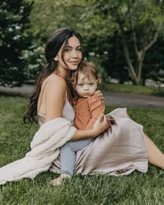 a woman sitting in the grass holding a baby