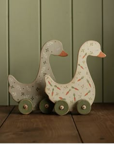 two wooden toy ducks sitting on top of a wooden table next to green wallpaper