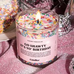 a pink candle with sprinkles on it and a cake in the background