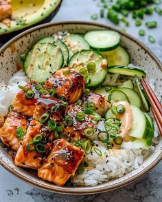 a bowl filled with rice, cucumber and salmon next to chopsticks