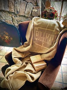 a chair covered with a blanket and two books sitting on top of it in front of a fireplace