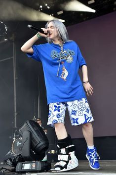 a man with grey hair and blue shoes on stage holding a microphone in his hand