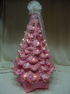 a pink christmas tree with white lights on it's base and a bow around the top