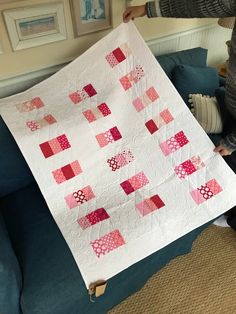 a woman holding up a quilt on top of a couch