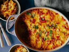 a casserole dish with cheese and vegetables in it next to two bowls on a blue surface