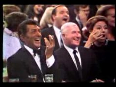 two men in tuxedos are laughing and clapping at an event with other people