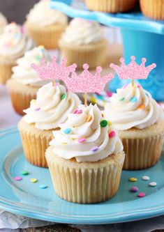 cupcakes with white frosting and pink crown toppers on a blue plate