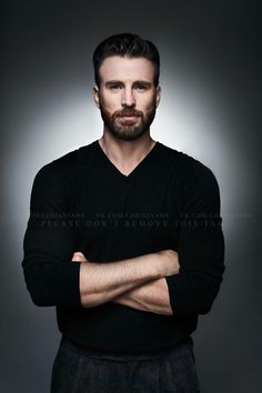 a man with his arms crossed posing for a photo in front of a dark background