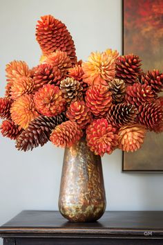 a vase filled with lots of pine cones on top of a wooden table next to a painting