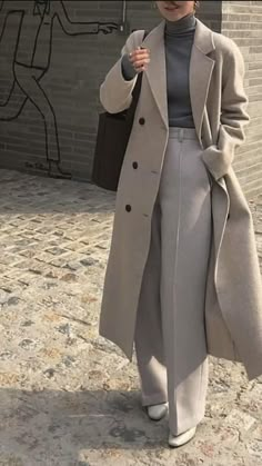 a woman is walking down the street with an umbrella in her hand and wearing a gray coat