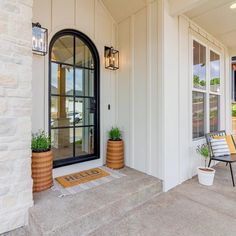 the front entrance to a home with two chairs and potted plants on the porch