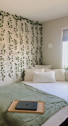 a bed with a laptop on top of it next to a wall covered in vines