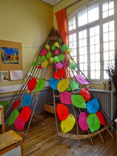 a teepee with colorful paper leaves hanging from it's sides in front of a window