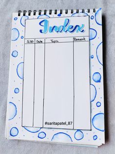 a spiral notebook with the words index written in blue water drops on it, next to a notepad