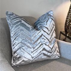 a blue and silver pillow sitting on top of a gray couch next to a lamp