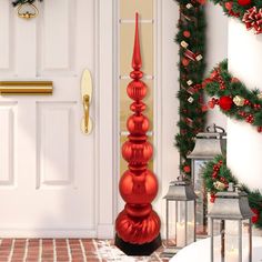 a tall red christmas tree sitting in front of a white door with decorations on it