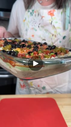 a woman is holding up a casserole dish with black olives and tomatoes