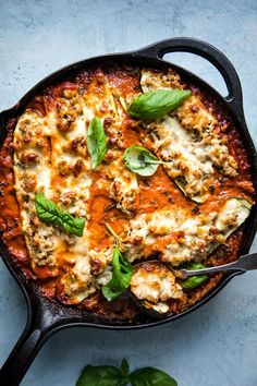 an iron skillet filled with lasagna sauce and basil garnished with cheese