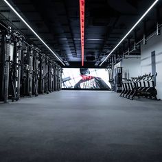 an empty gym with rows of machines and lights on either side of the room that is lit up