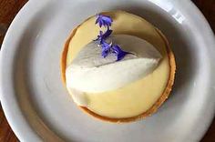 a small dessert on a white plate with blue flowers in the center and purple petals sticking out of it