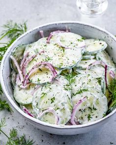 a bowl filled with cucumbers and onions on top of a white tablecloth