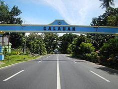 an open road with a blue sign that says cauaun on the side and trees in the background