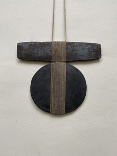 a piece of wood and metal hanging from a string on a white wall next to a black circle