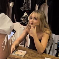 a woman sitting at a table in front of some shirts