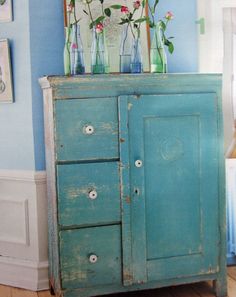 an old blue cabinet with flowers in vases on top