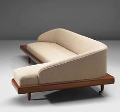 a couch and ottoman sitting on top of a wooden stand in front of a gray wall