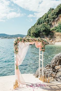 an outdoor wedding setup on the beach with pink flowers and greenery draped over it