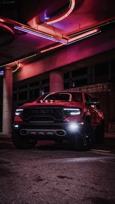 a red truck parked in front of a building with neon lights on it's sides