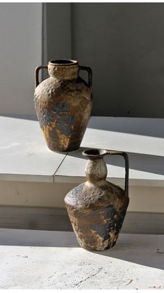 two old vases sitting on the ground next to each other in front of a window