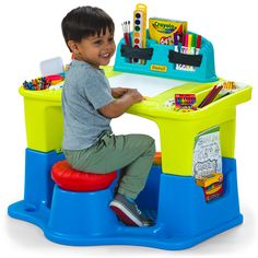 a young boy sitting at a desk with markers and pencils