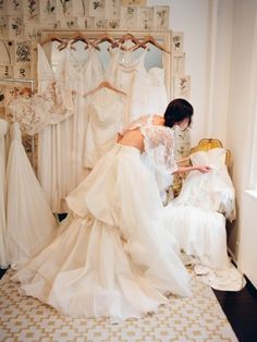 a woman in a white wedding dress looking at dresses