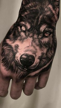 a person's hand with a wolf tattoo on it, showing the face and eyes