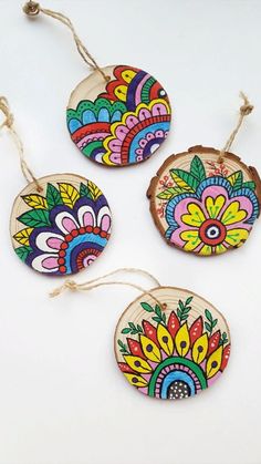 three wooden ornaments with colorful designs hanging from twine strings on a white table top