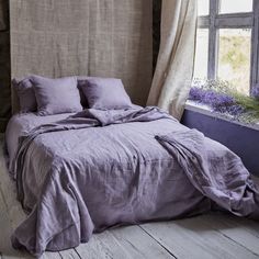 an unmade bed in front of a window with lavender flowers on the windowsill