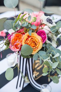 a vase filled with lots of flowers on top of a table covered in black and white stripes