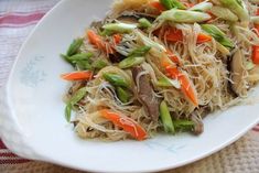 a white plate topped with noodles and veggies on top of a checkered table cloth