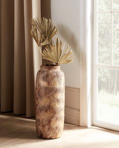 a vase with some plants in it on the floor next to a window sill