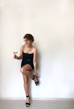 a woman in a short black dress holding a wine glass and posing for the camera