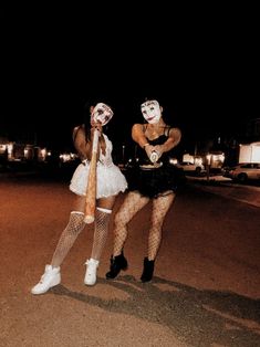 two women dressed up as clowns in the street at night with one holding a bat