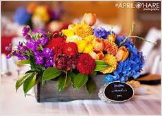 an arrangement of colorful flowers in a wooden box with a chalkboard sign on the table