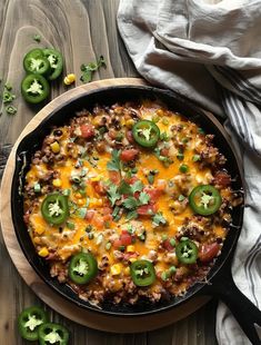 a skillet filled with mexican food on top of a wooden table next to green peppers and jalapenos